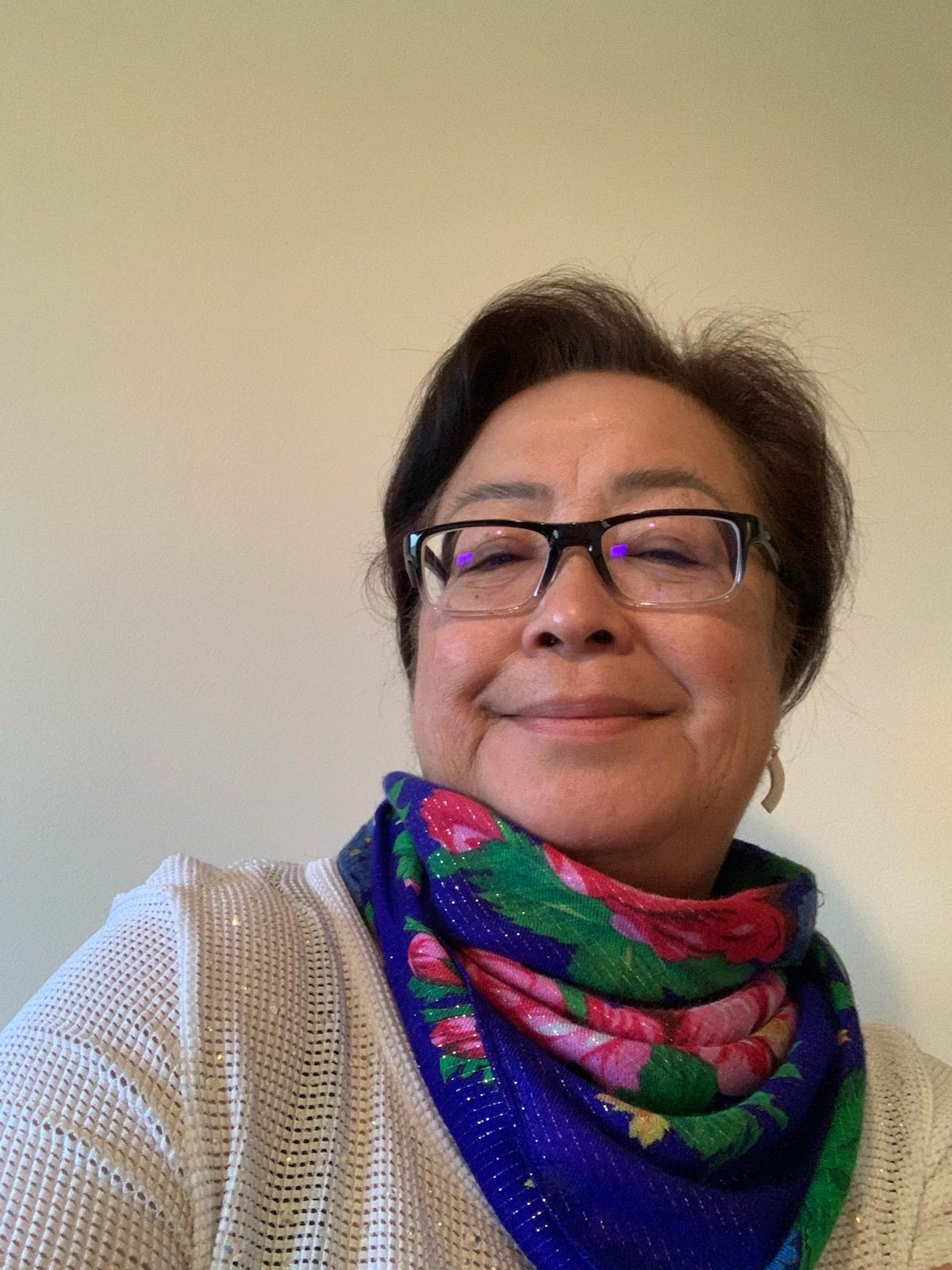 Woman wearing glasses and a colorful floral scarf, smiling while posing against a plain background.